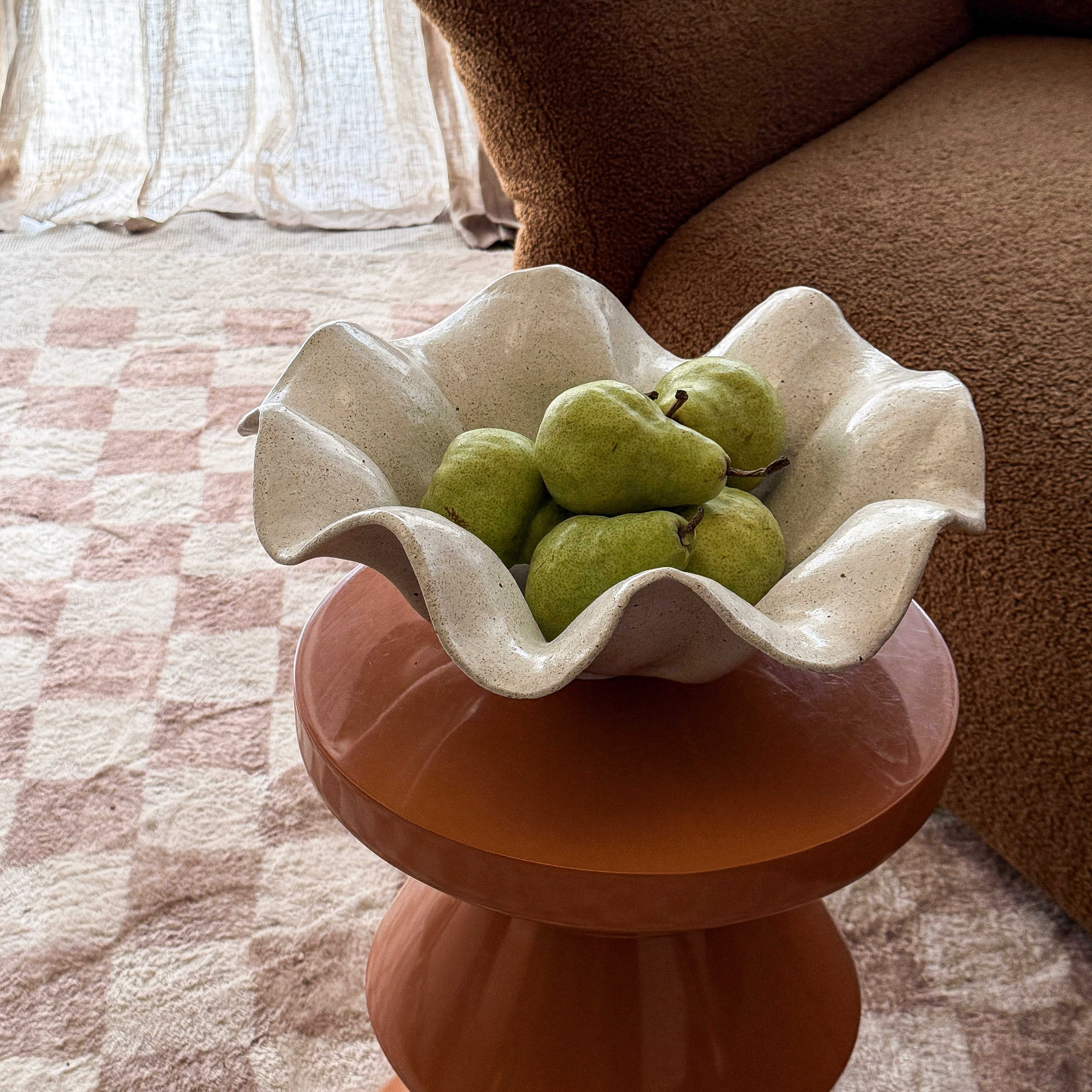 White ceramic bowl with green pears on a wooden side table in a living room.